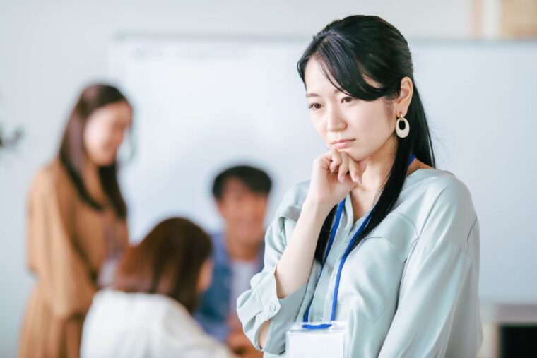 職場で戸惑いの表情を浮かべる女性。周囲の指導に振り回され、自信をなくしかけている。
